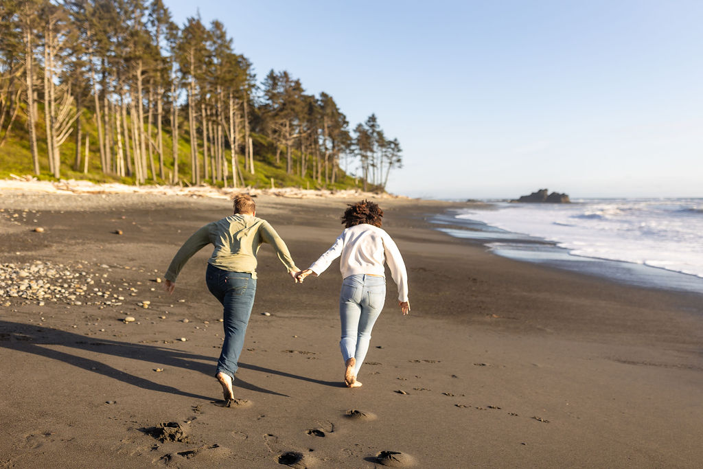 couple holding hands running at the beach 