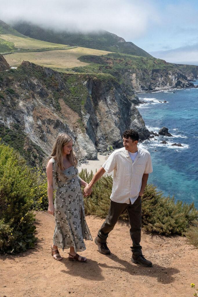 couple holding hands walking around bixby bridge 